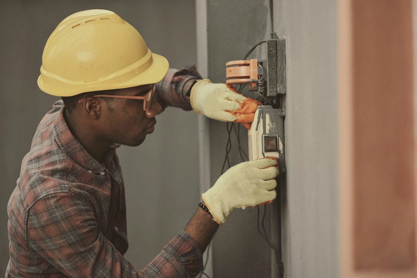 An electrician in a hard hat testing wiring at a wall panel