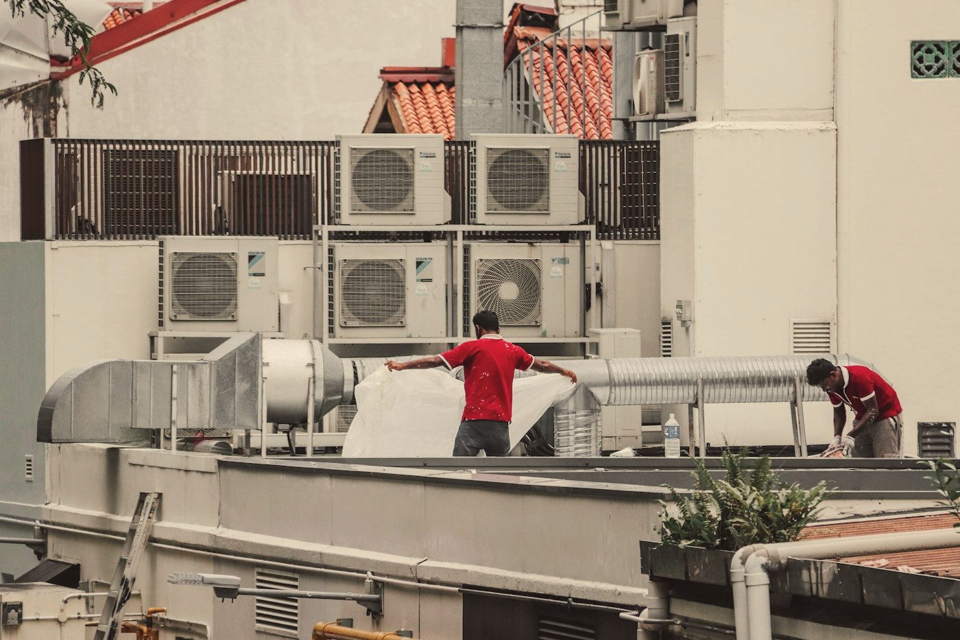 Two technicians working among air-conditioning units on a rooftop