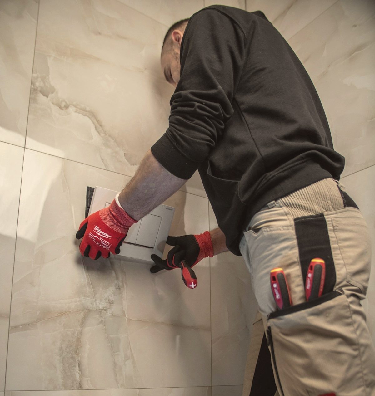 A plumber fitting a toilet flush plate in a tiled bathroom